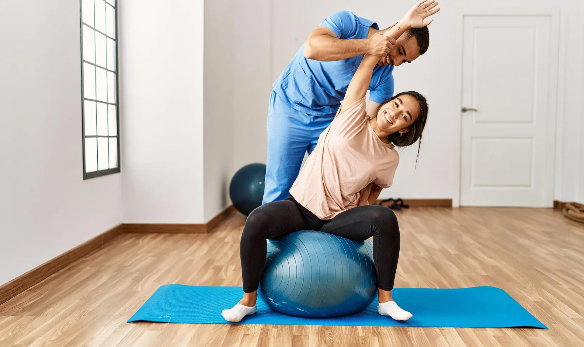 Bewegungstherapie im Reha-Zentrum Alland – Physiotherapeut unterstützt Patientin bei Dehnübung auf Gymnastikball